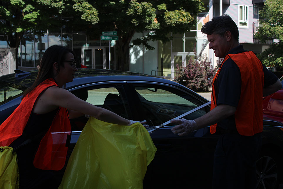 2 Atlas employees helping each other pick up trash from the street and put it into a bag